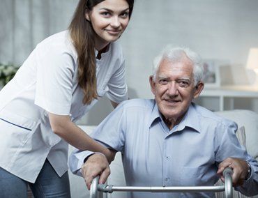 A female nursing helping an elderly man stand up out of his chair