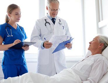 A doctor and a nurse reading from clipboards talking to a patient in a hospital bed