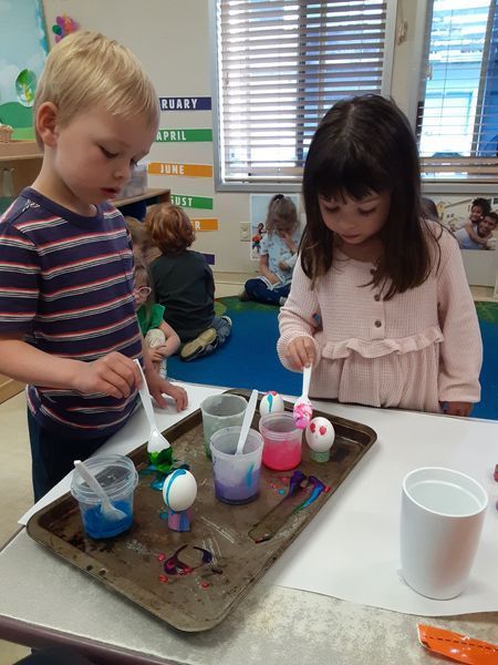 Two children painting Easter eggs in a classroom.