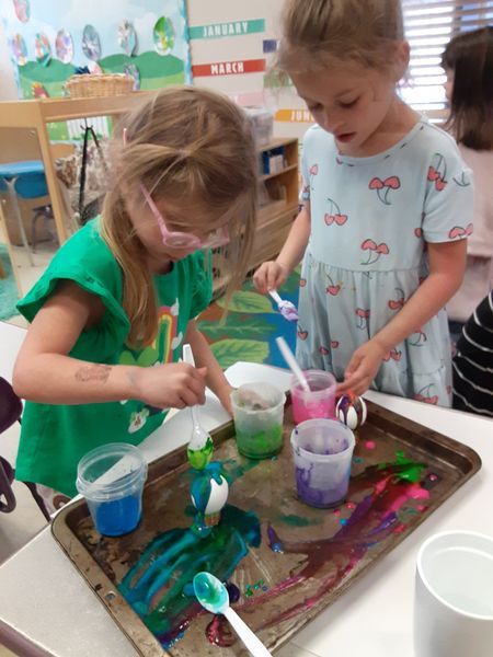 Two young children painting with colorful liquids at a table in a classroom.