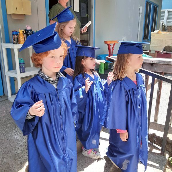 Children in blue graduation gowns and caps, standing outside a building.