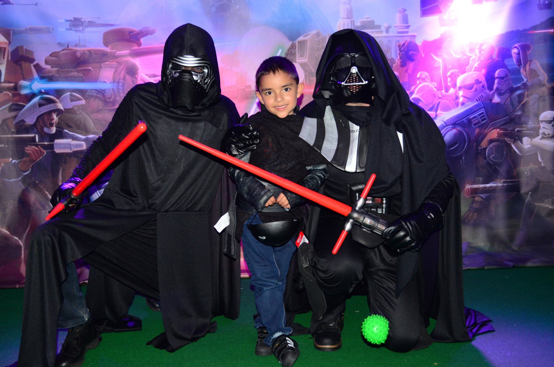Un niño pequeño posa para una foto con dos hombres vestidos como Darth Vader y Kylo Ren.