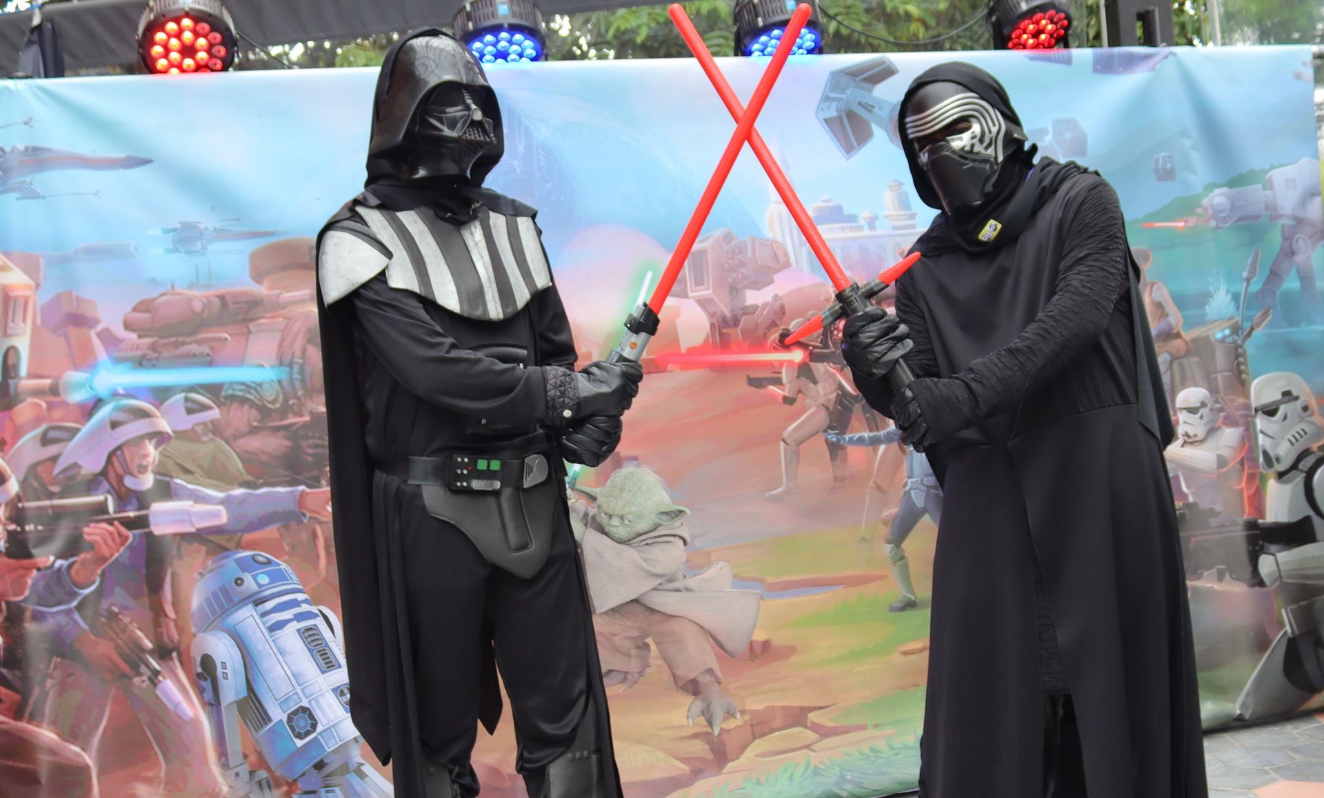 Dos hombres vestidos como Darth Vader y Kylo Ren sostienen sables de luz.