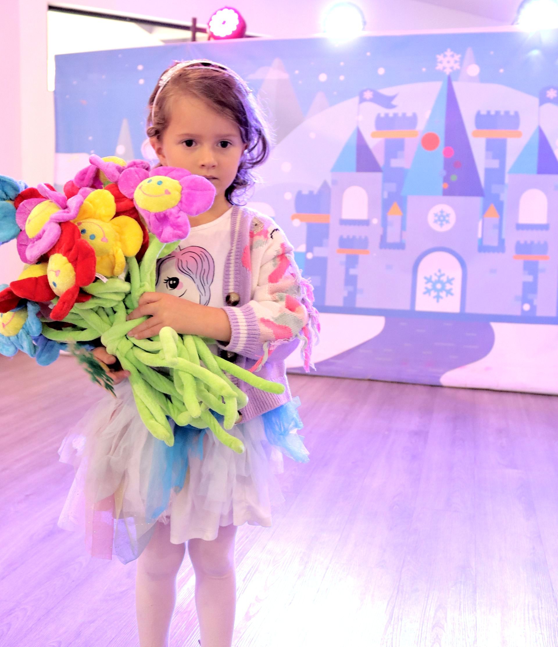 Una niña sostiene un montón de animales de peluche frente a un castillo.