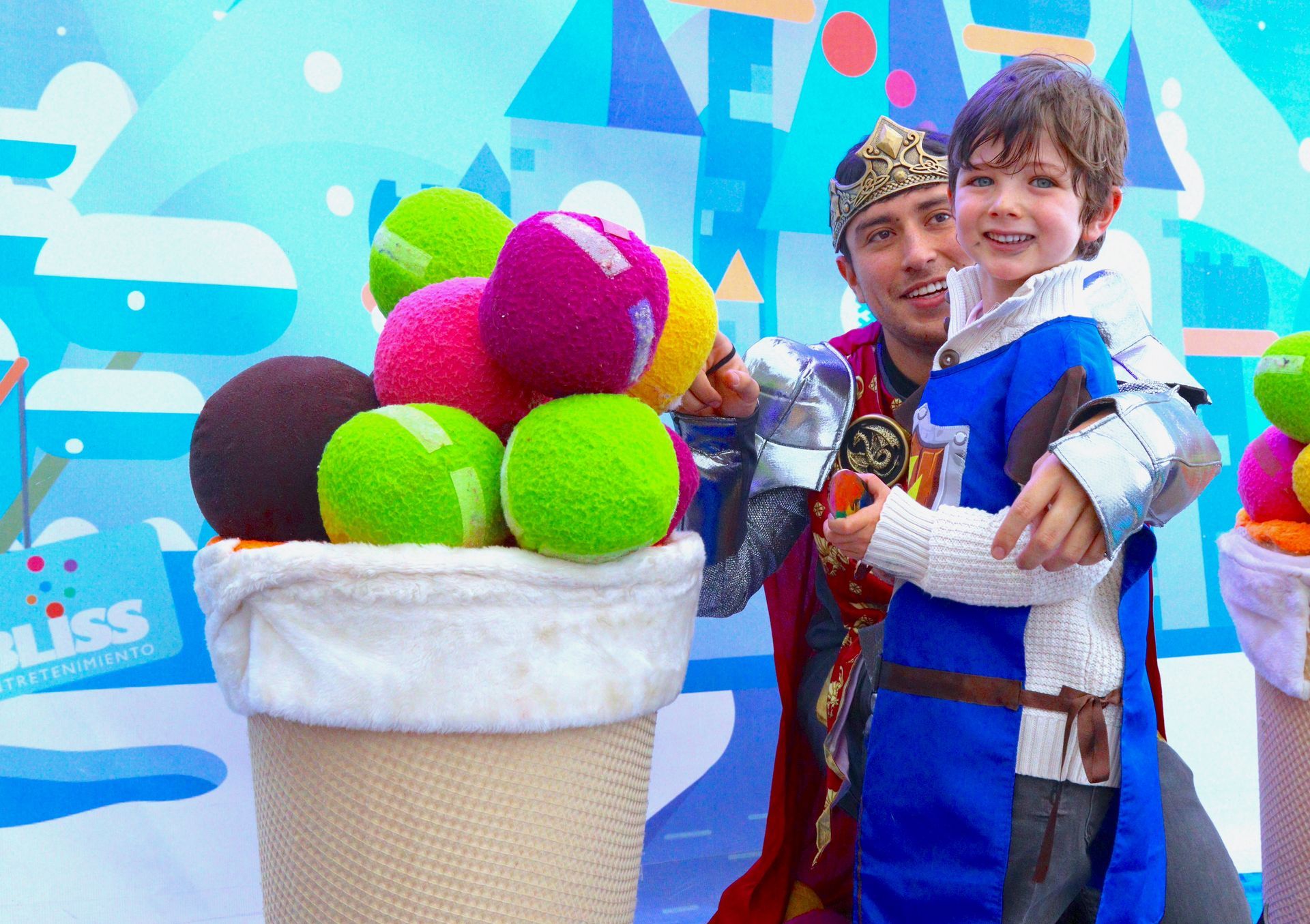Un hombre y un niño están de pie junto a un cono de helado lleno de pelotas de tenis.