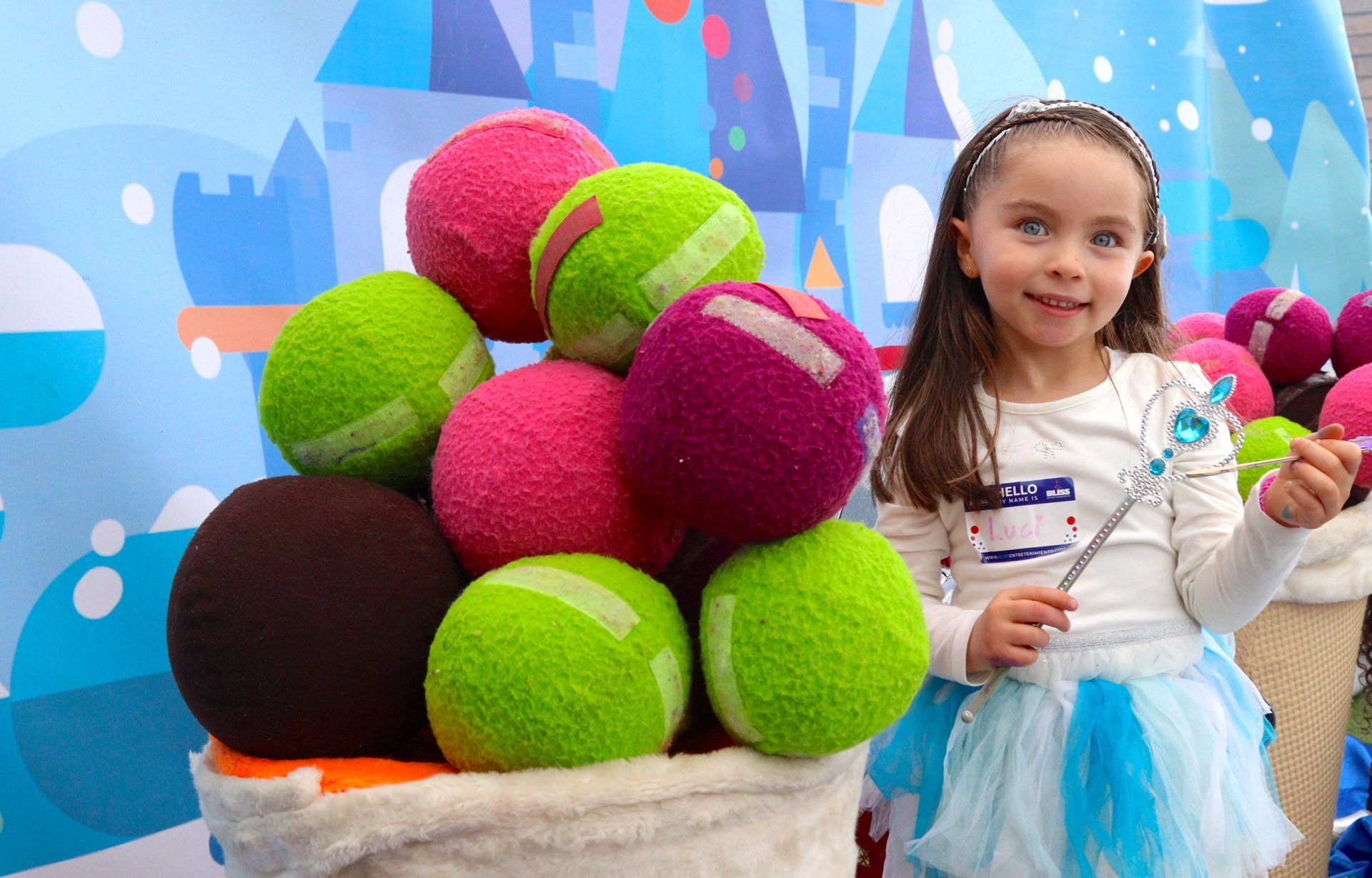 Una niña está parada junto a una canasta llena de pelotas de tenis.