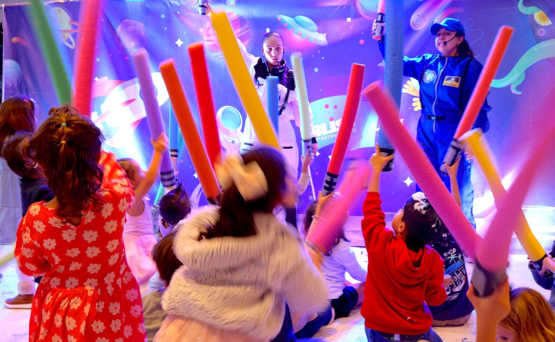 Un grupo de niños sostiene palos de espuma frente a un escenario.