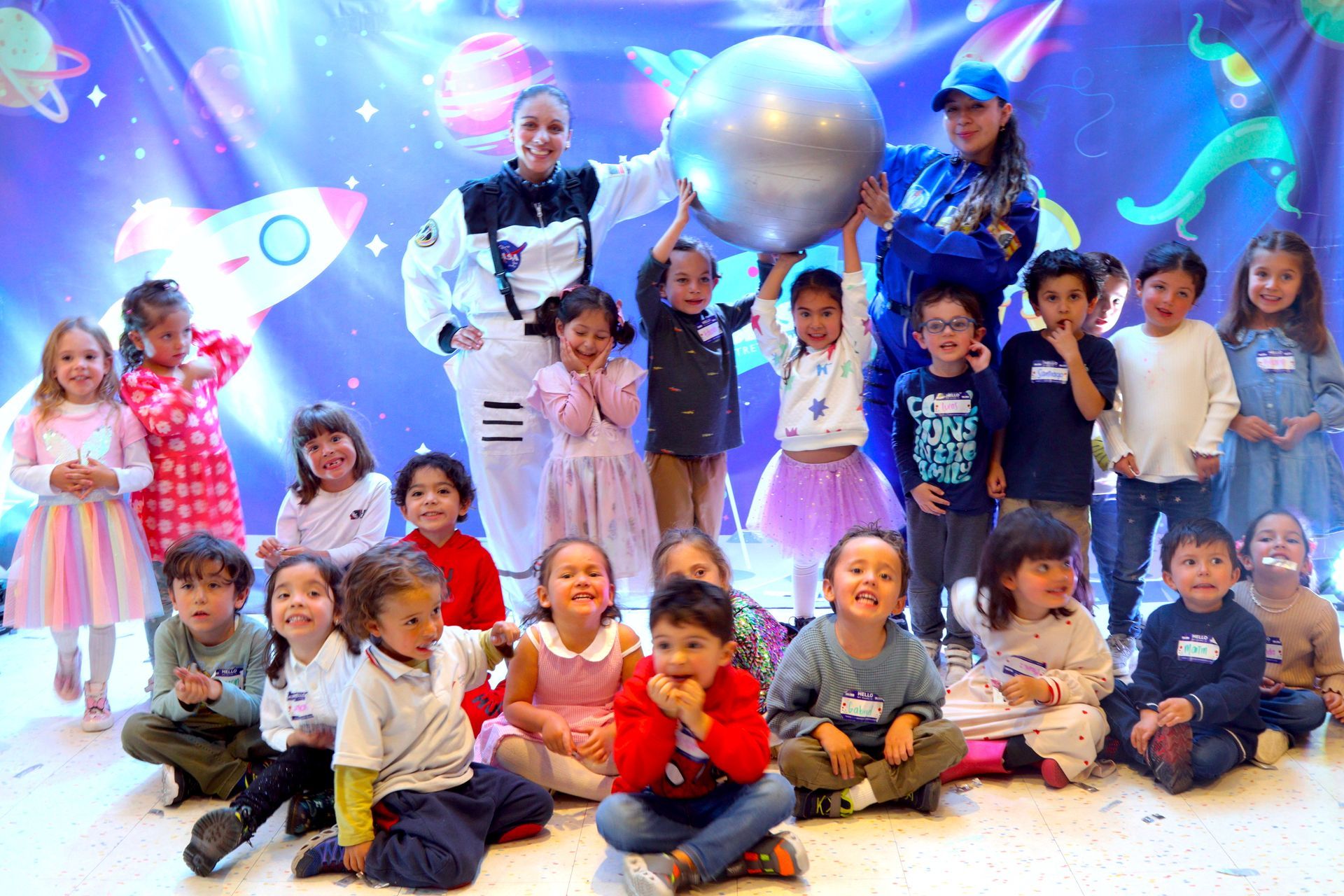 Un grupo de niños posan para una fotografía mientras están sentados en el suelo.