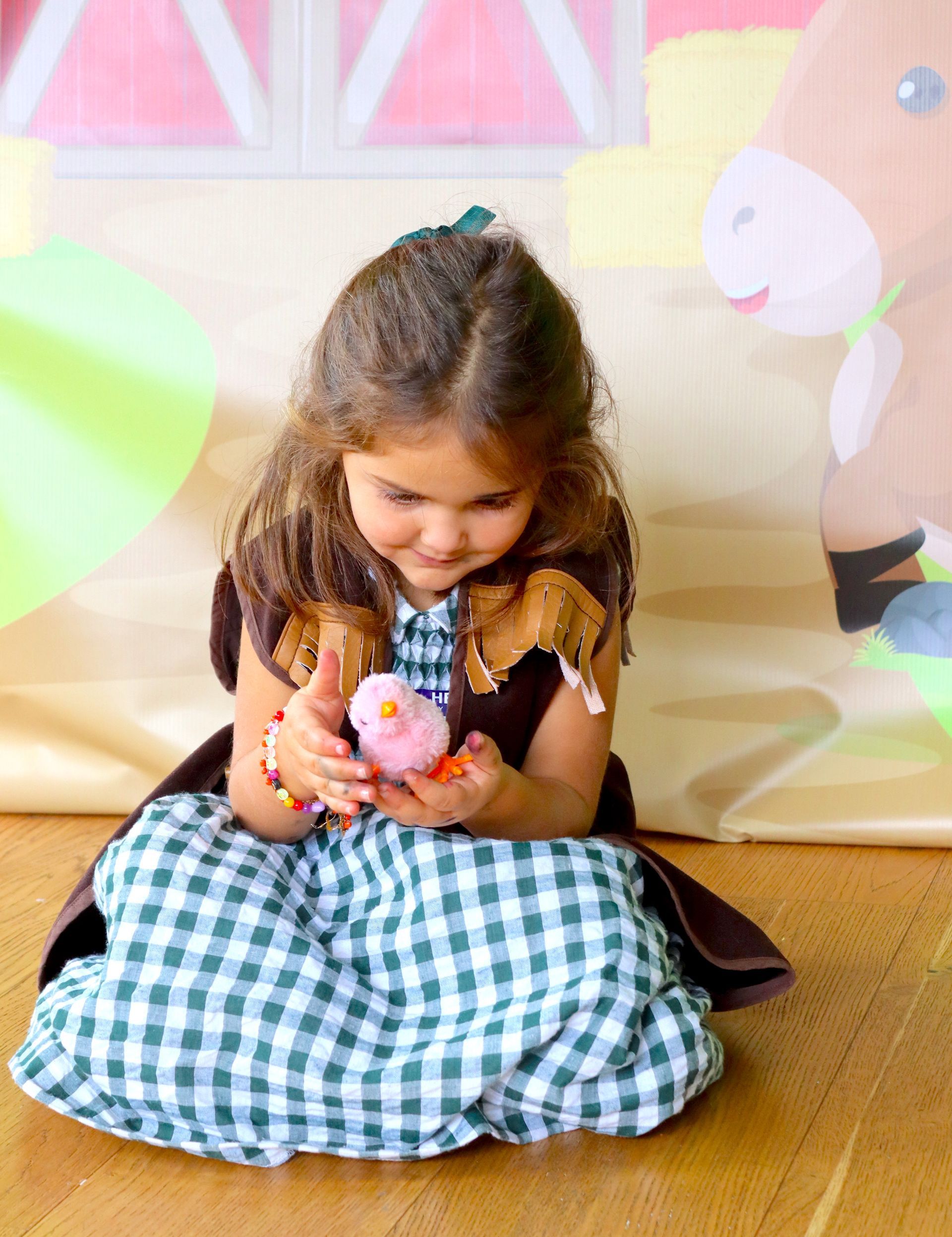 Una niña con un vestido está sentada en el suelo sosteniendo un animal de peluche.