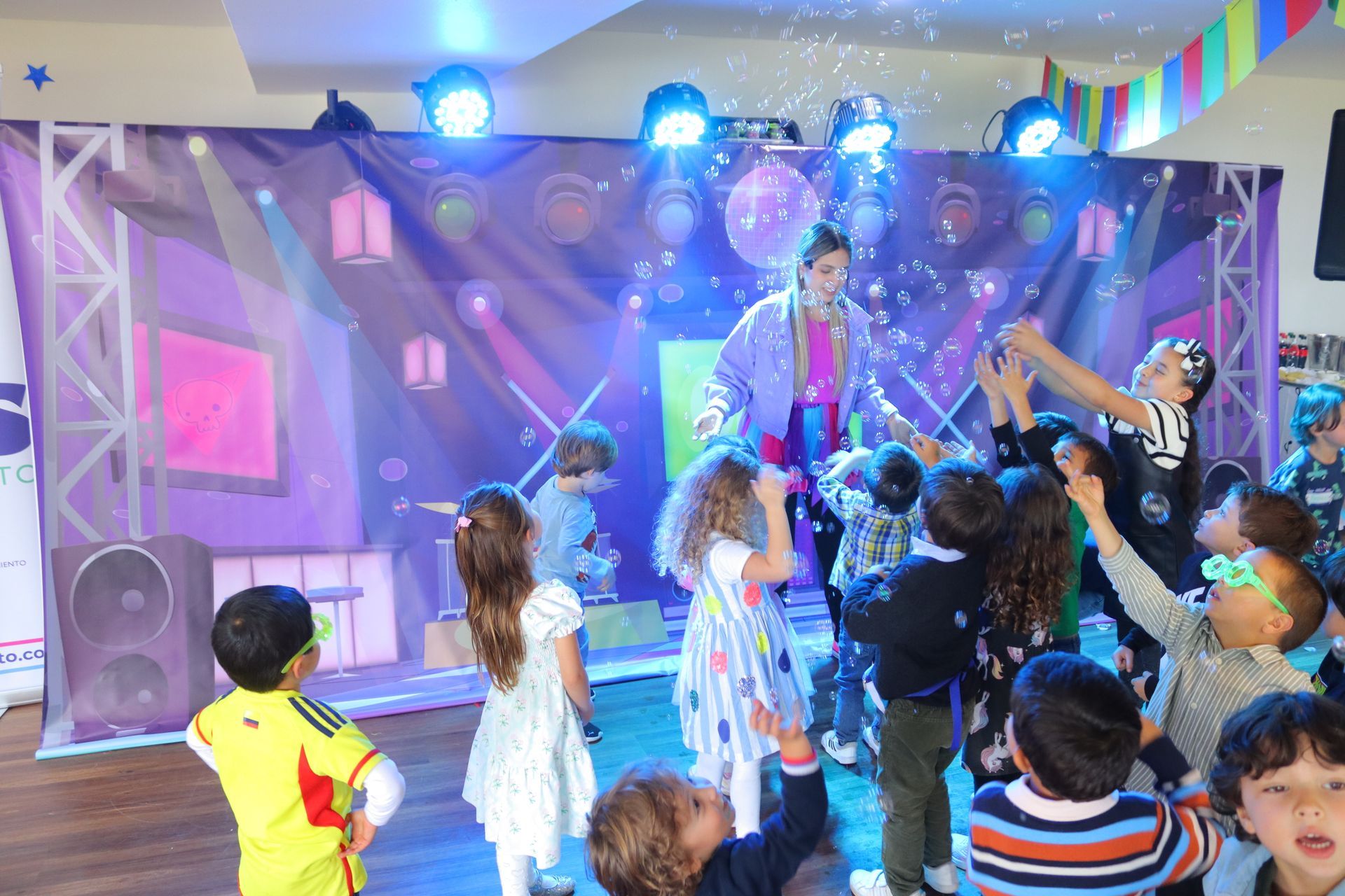 Un grupo de niños está bailando frente a un escenario en una fiesta.