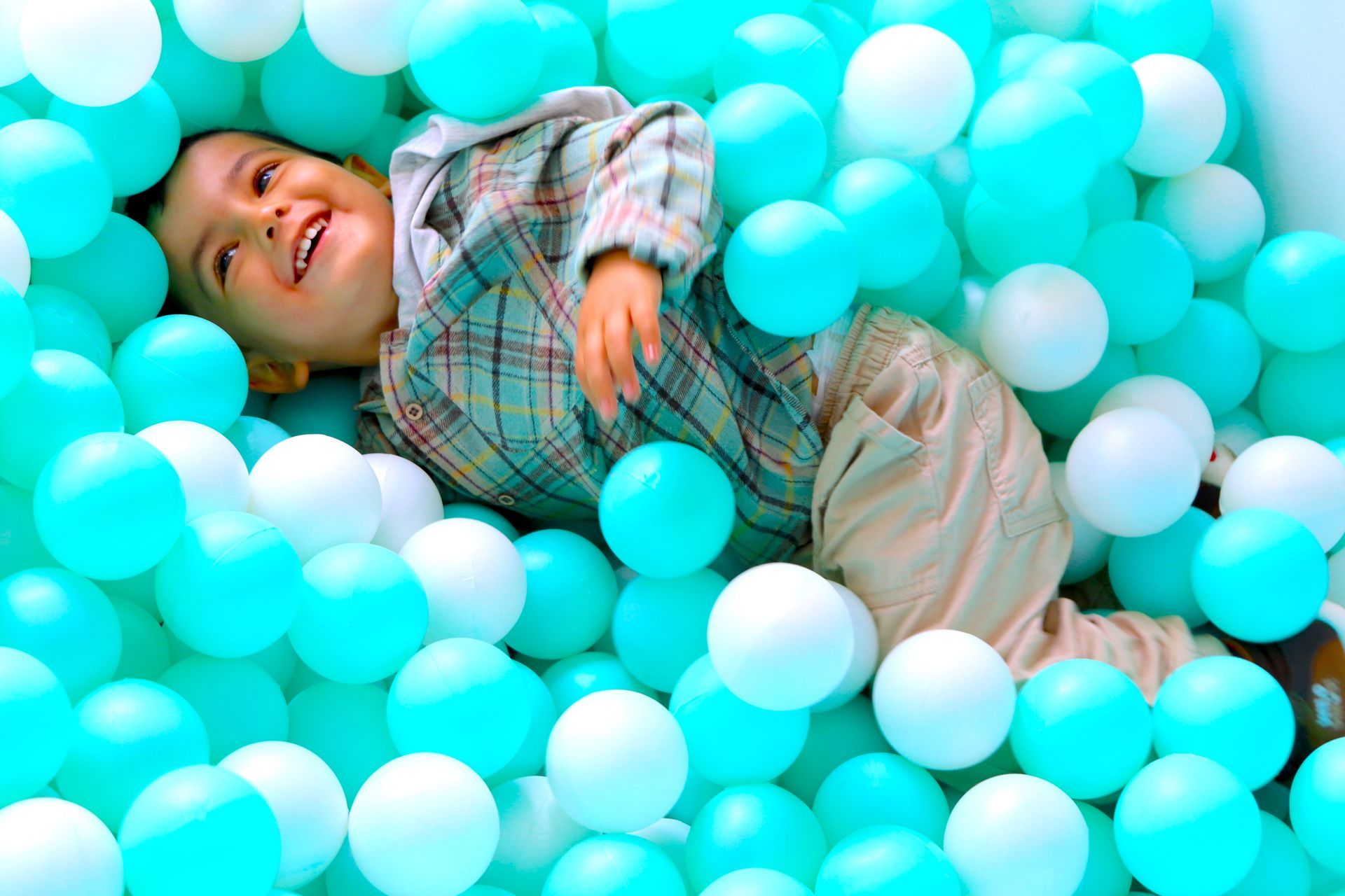 Un niño pequeño está acostado en una piscina de pelotas llena de pelotas azules y blancas.