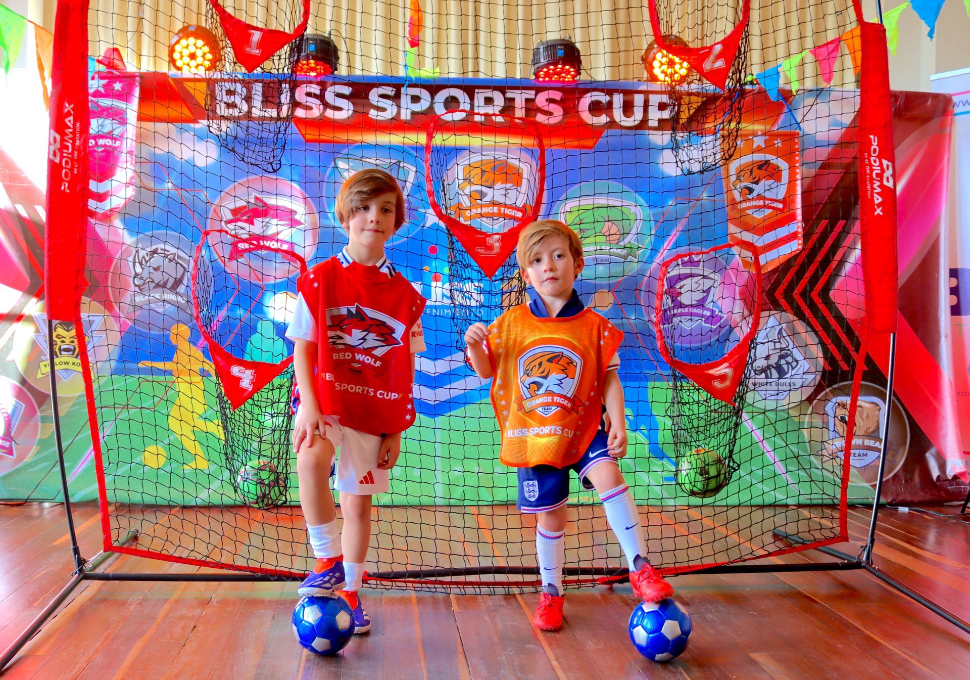 Dos niños pequeños están parados uno al lado del otro con pelotas de fútbol frente a una pared.