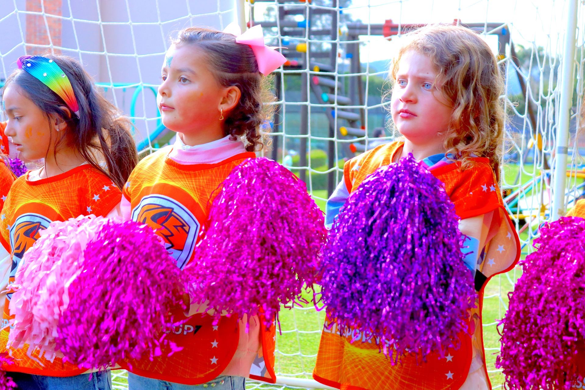 Un grupo de chicas jóvenes están animando con pompones rosas y morados.