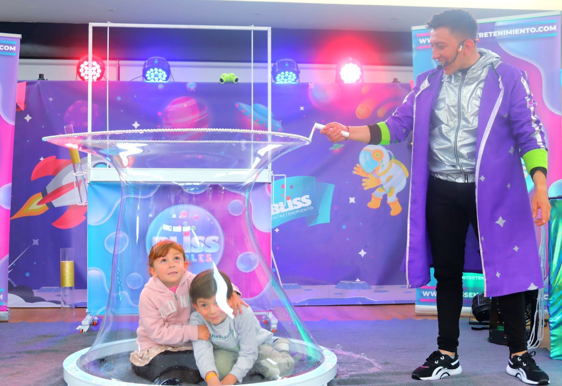 Un hombre con un abrigo morado está jugando con dos niños en una burbuja de jabón.