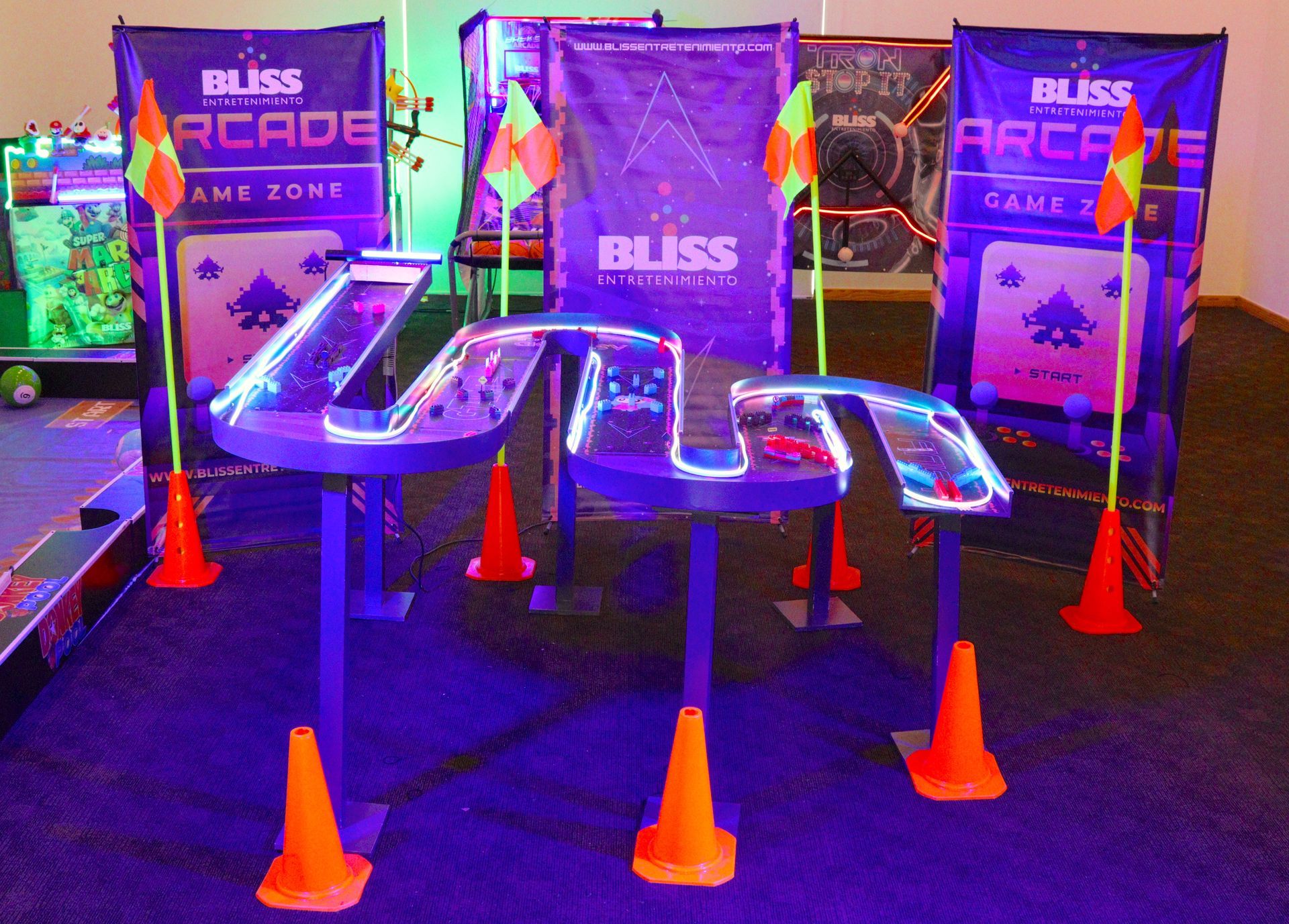 Juego arcade de luz negra con una pista sinuosa y brillante, conos naranjas y carteles de 