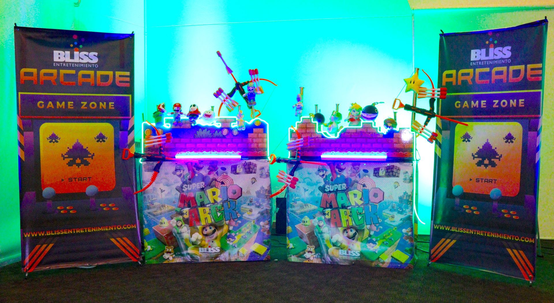 Zona de juegos arcade con máquinas bien iluminadas, arte colorido y pancartas. Iluminación azul y verde.