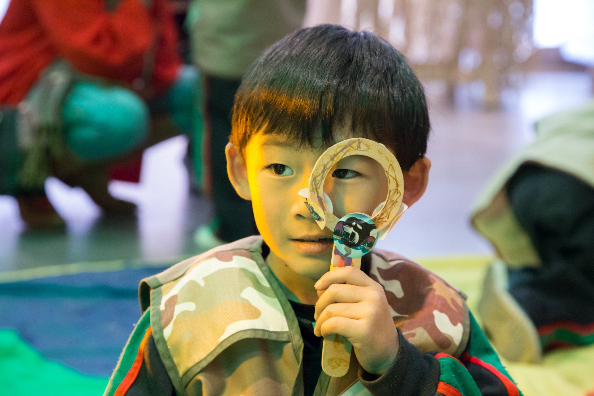 Un niño pequeño sostiene una lupa delante de su cara.