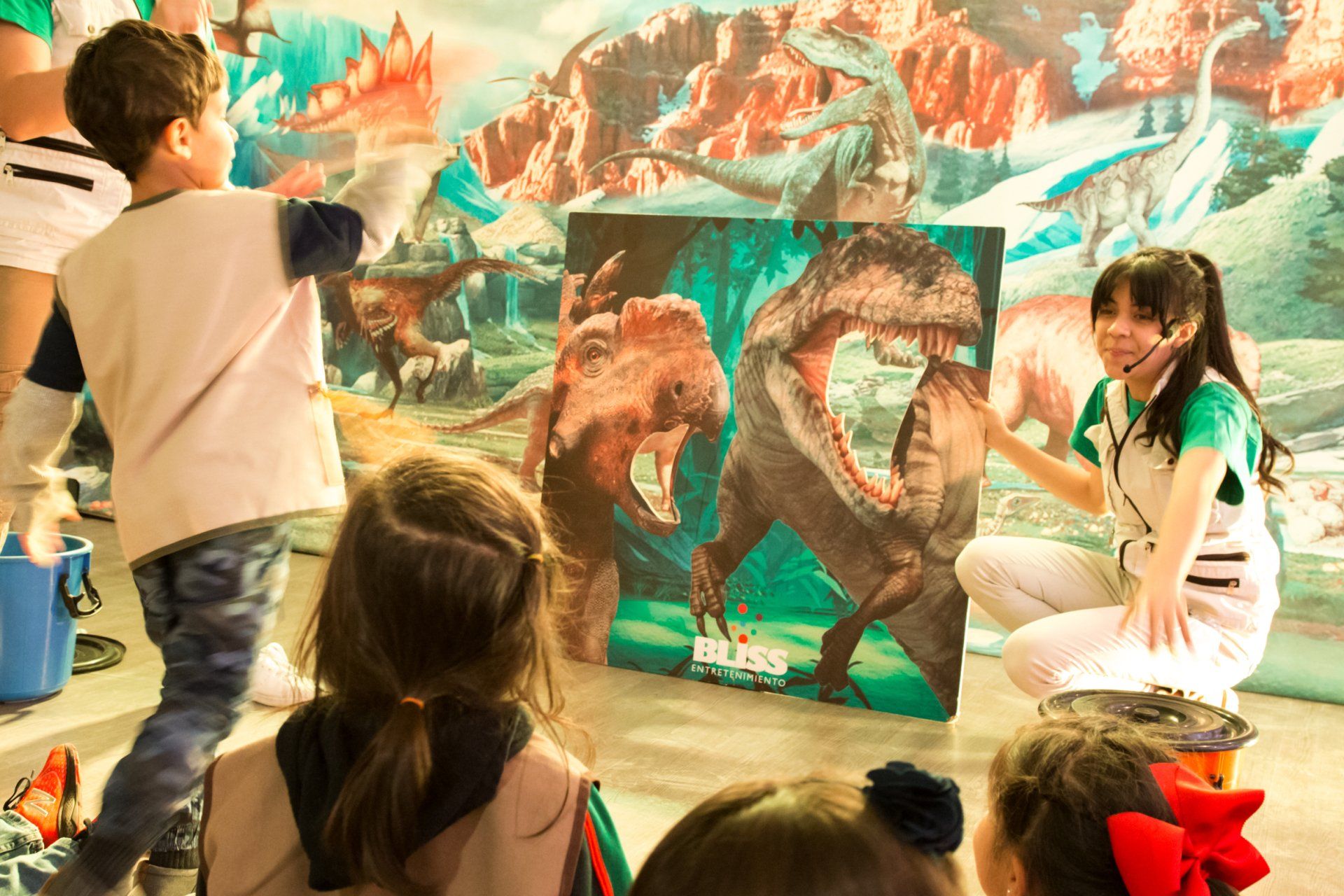 Un grupo de niños está sentado frente a un cuadro de dinosaurios.