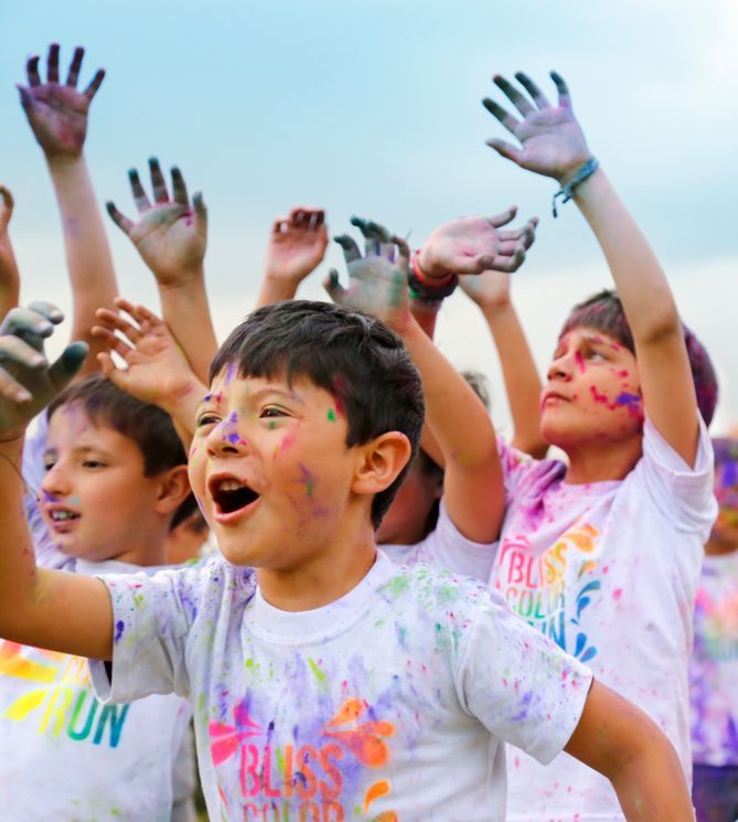 Los niños cubiertos de polvo de colores levantan sus manos, celebrando una carrera de colores.