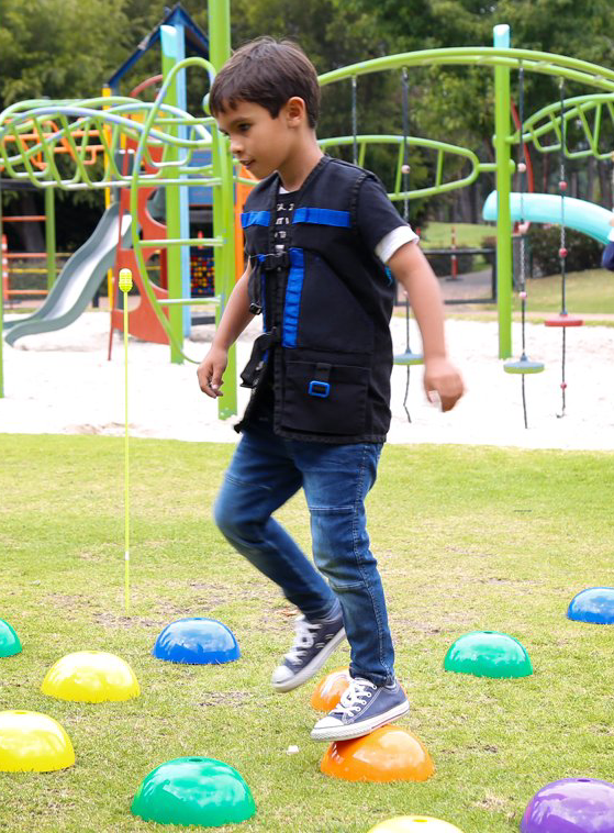 Un niño pequeño está parado sobre una fila de conos de colores en un parque.