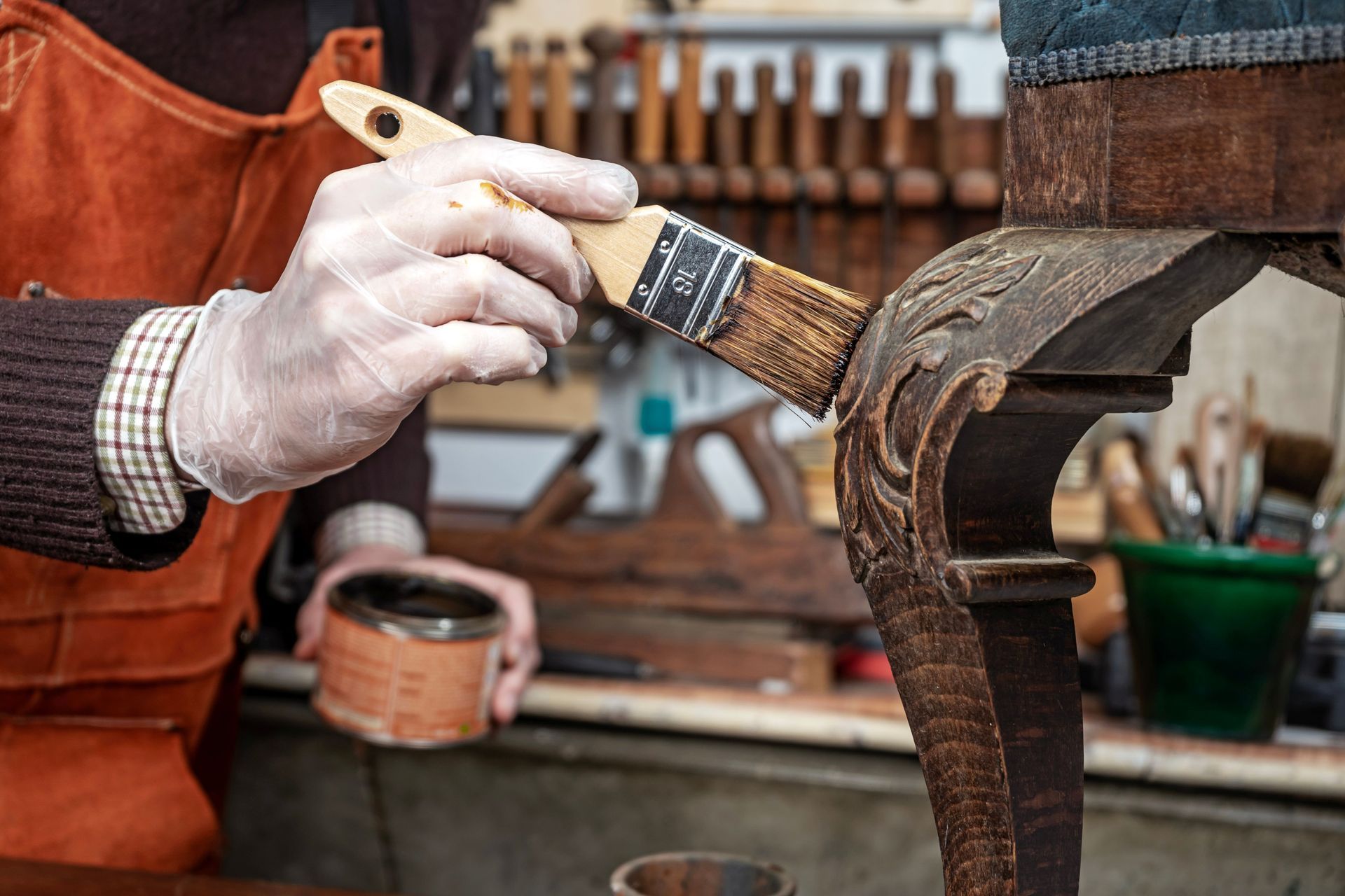 A partial view of a carpenter restoring an antique chair with wood wax and a brush.