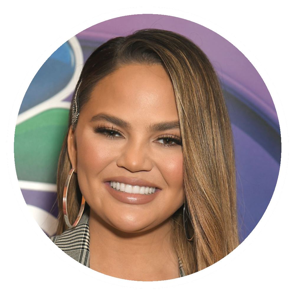 Chrissy Teigen smiling, wearing hoop earrings, with long, straight hair, posing in front of a colorful backdrop.