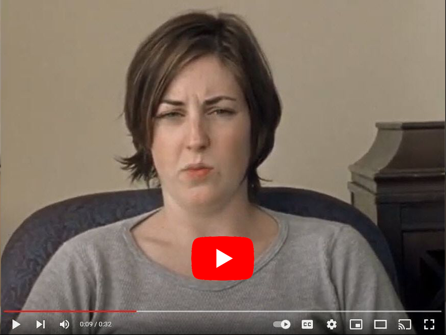 Woman with a skeptical expression seated indoors, wearing gray shirt, with play button overlay.