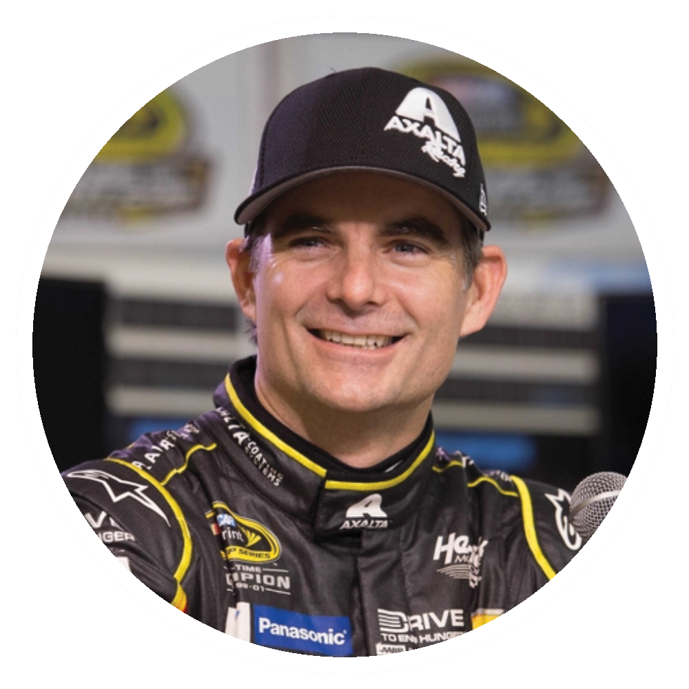 Jeff Gordon in a racing uniform and hat smiling, with a black and yellow jacket and logo details.