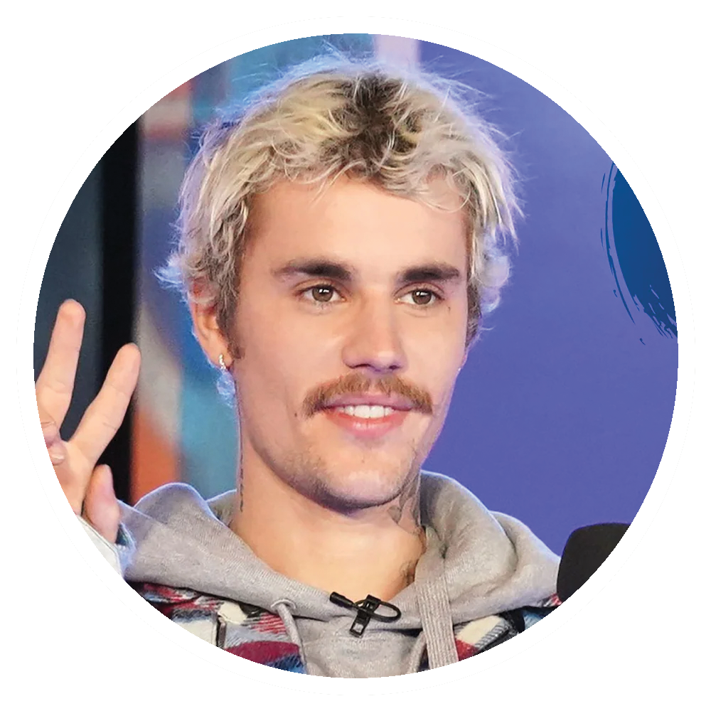 Justin Bieber with blonde hair and a mustache, smiling and gesturing.