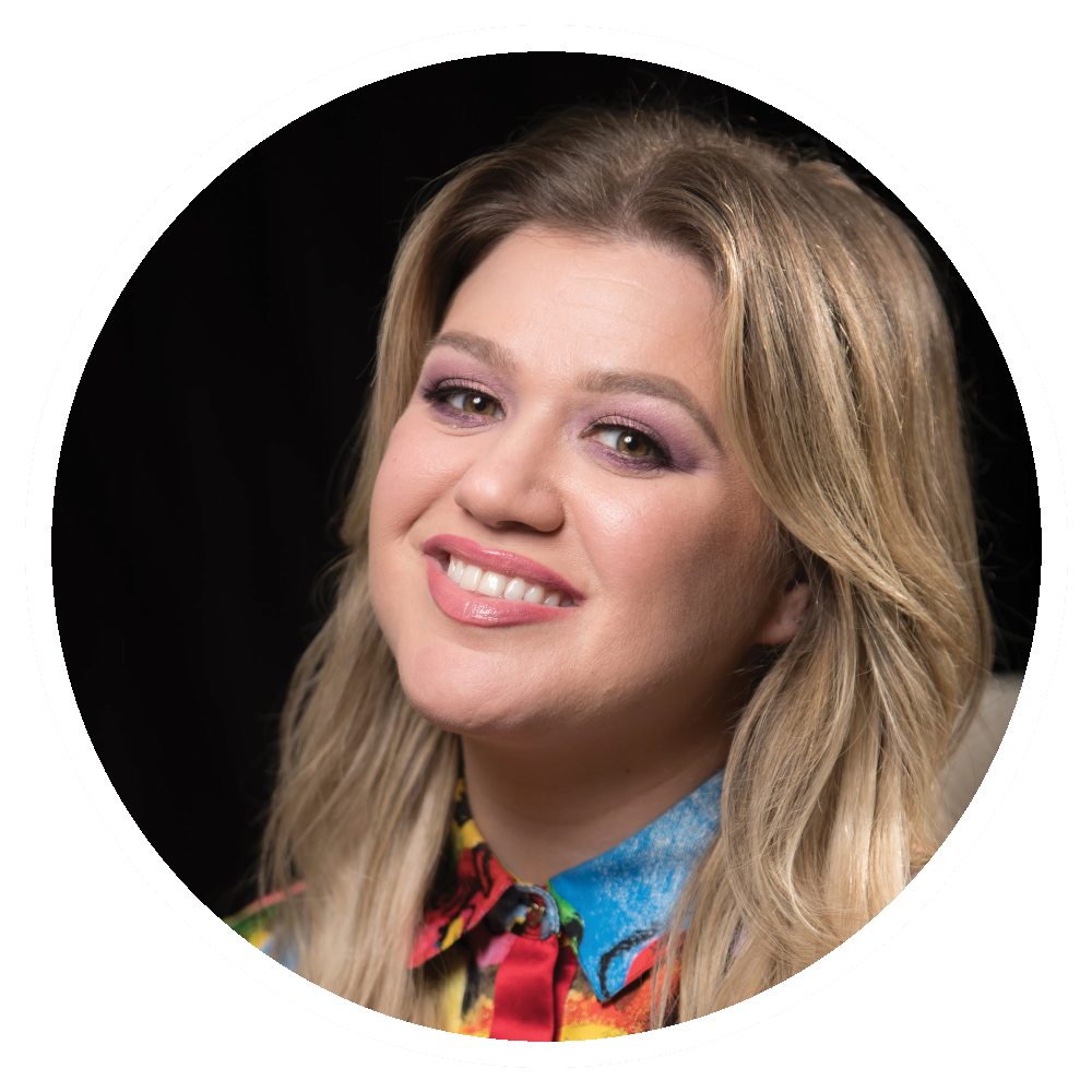 Kelly Clarkson smiles, wearing a colorful shirt and light eyeshadow, set against a black backdrop.