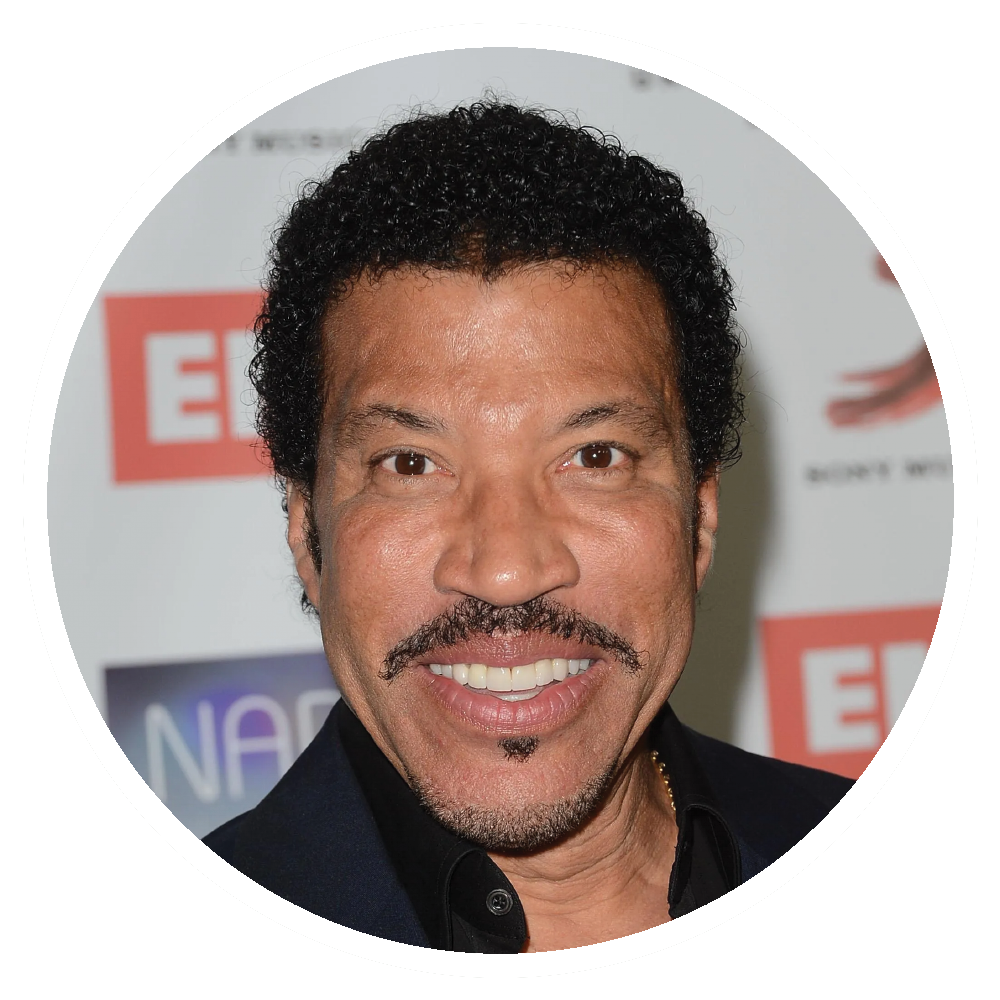 Lionel Richie smiling, wearing a dark suit, set against a blurred background.