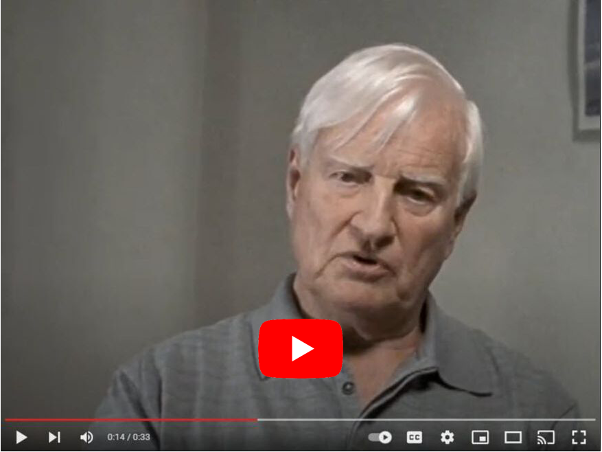 Man with white hair in a gray shirt speaking, with a YouTube video play button overlay.