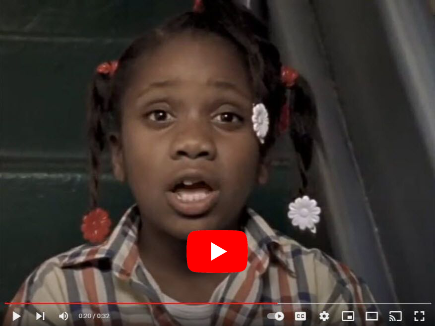 Young girl speaking, wearing a plaid shirt and flower hair accessories.