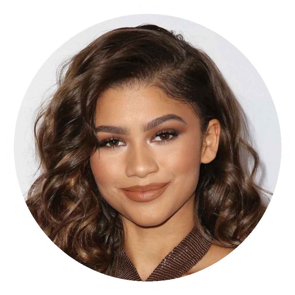 Zendaya with brown, curly hair, wearing makeup, smiling.