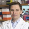 A man in a lab coat is smiling for the camera.