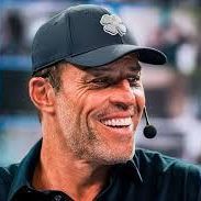 A man wearing a baseball cap and a microphone is smiling.