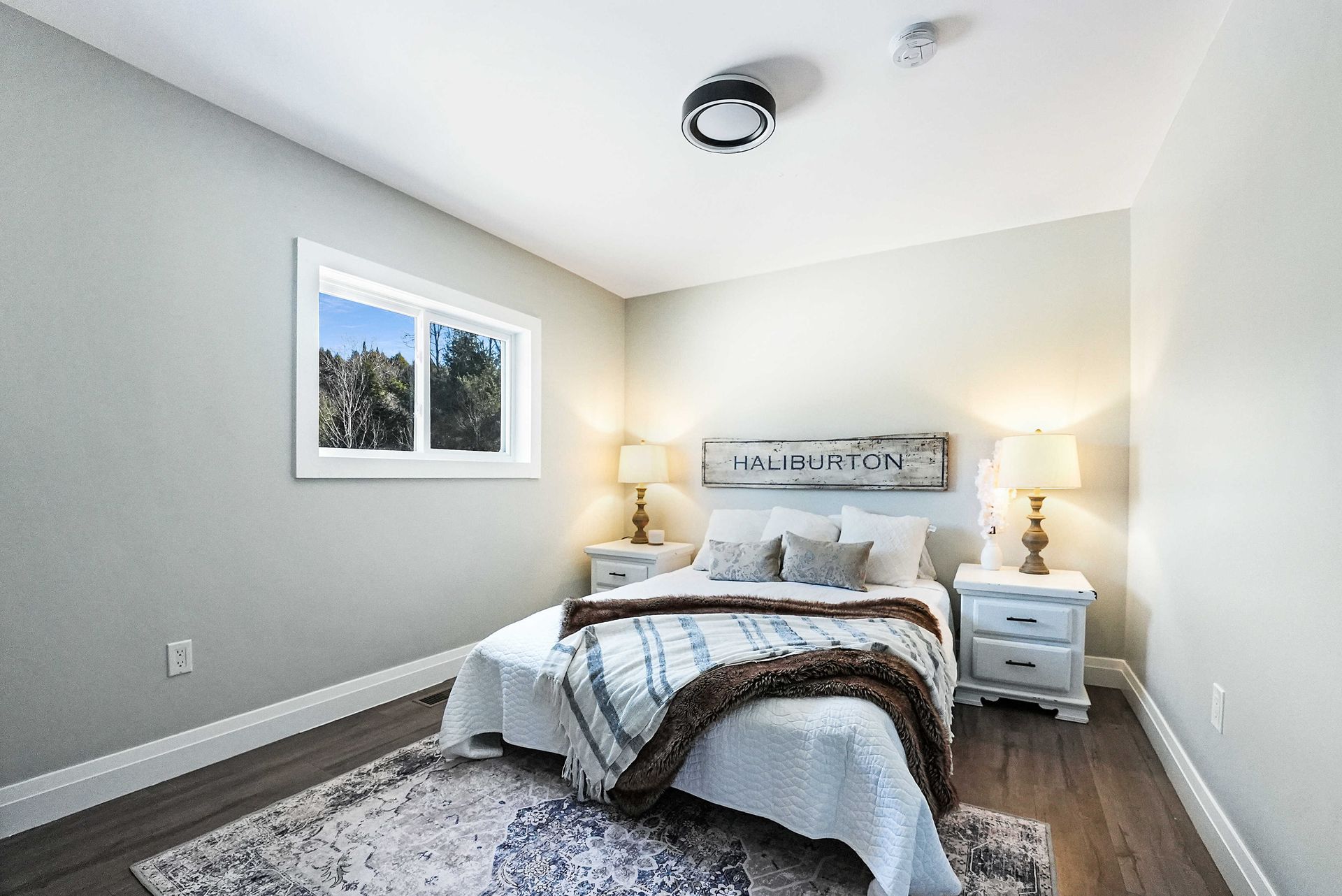 Bedroom with bed, nightstands, window, rug, and warm lighting.