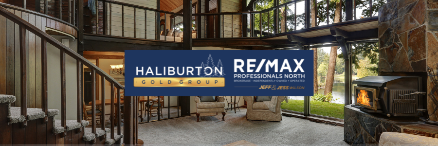 Interior view of a house with a fireplace, staircase, and large windows. The RE/MAX Haliburton Gold Group logo is in the foreground.
