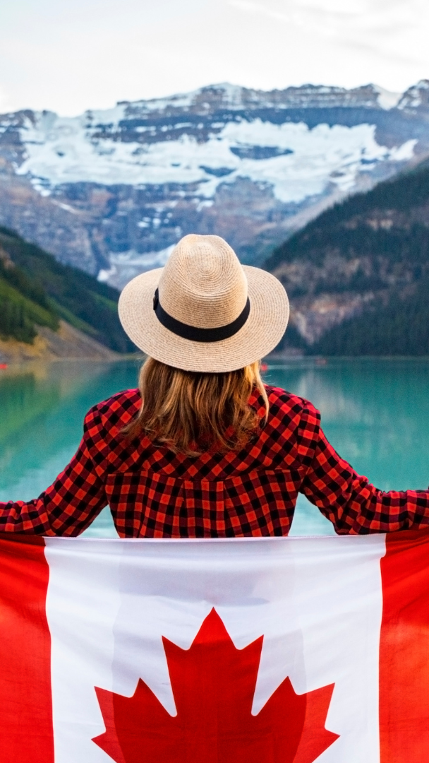 A woman is holding a canadian flag in front of a lake.