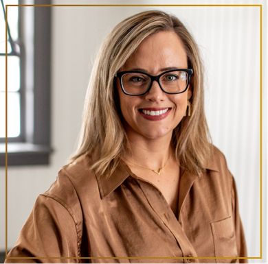 A woman wearing glasses and a brown shirt is smiling for the camera.