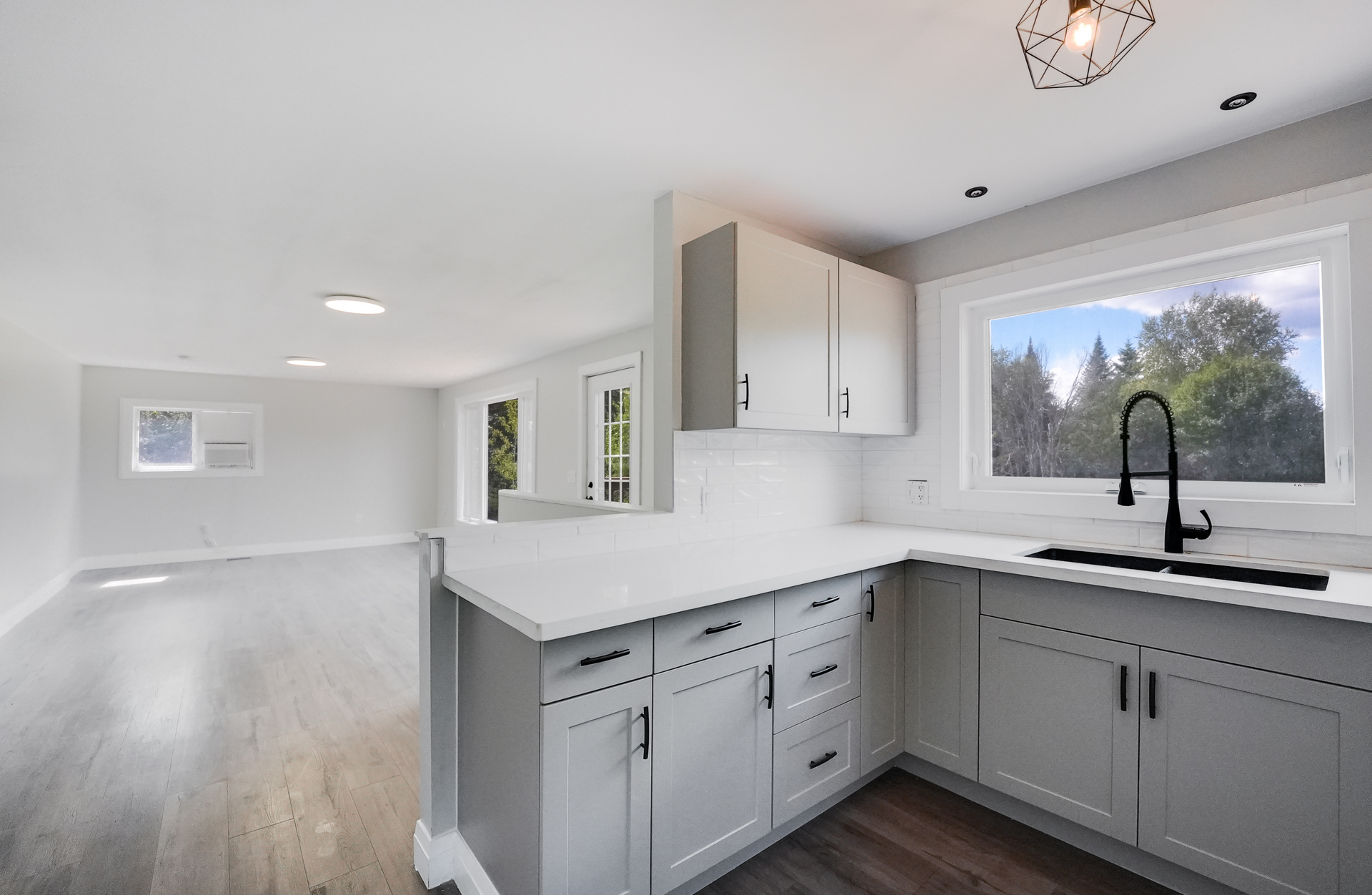 Modern, renovated kitchen with light gray cabinets, white countertops, and open concept to living space.