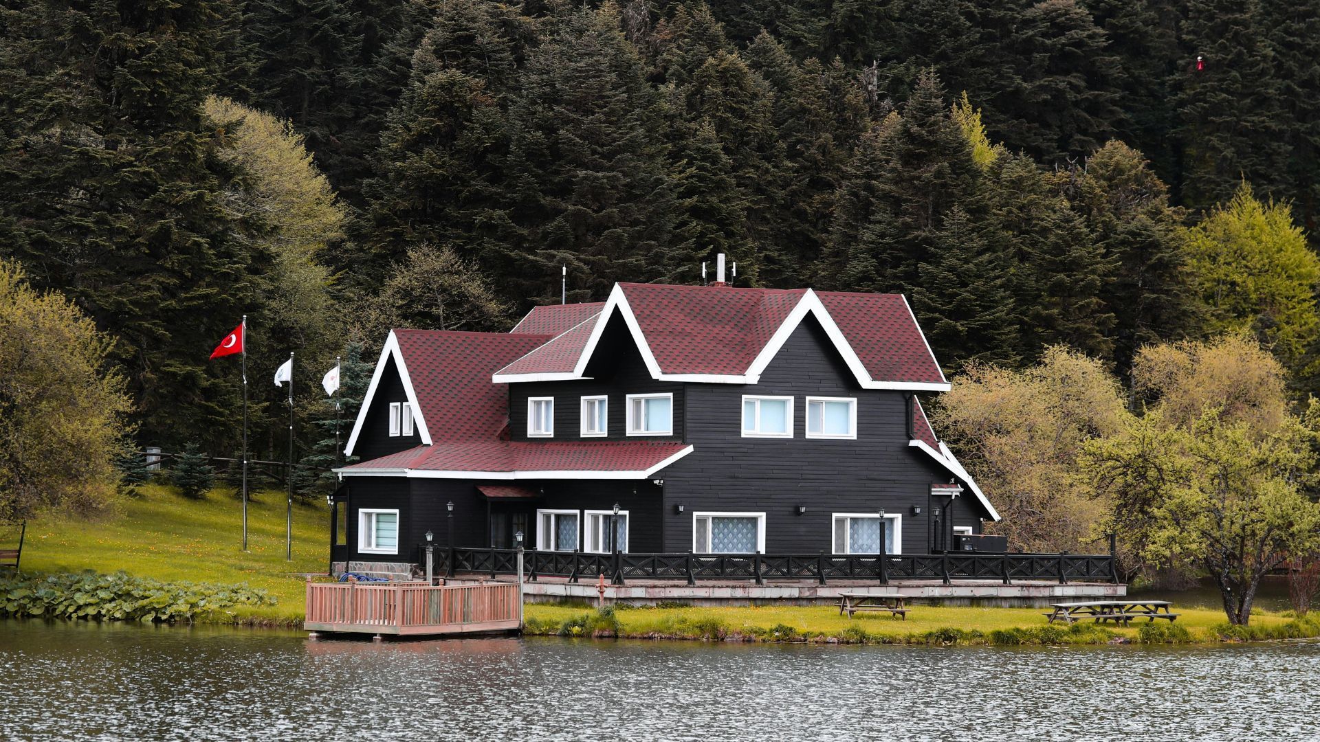 Dark lakeside house with a red roof, white trim, and a small dock by the water, backed by trees.