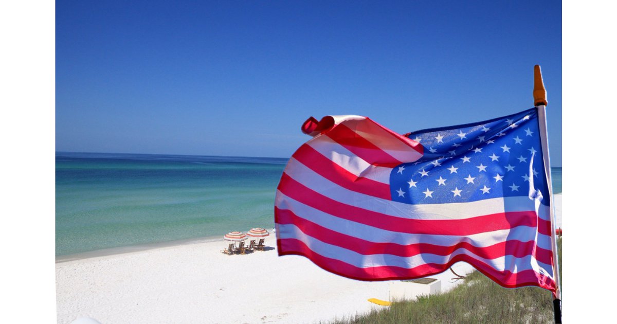 Two american flags are waving in the wind on a beach