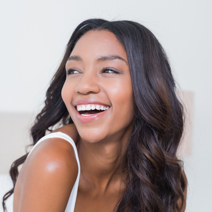 A woman with long dark hair is smiling and wearing a white tank top