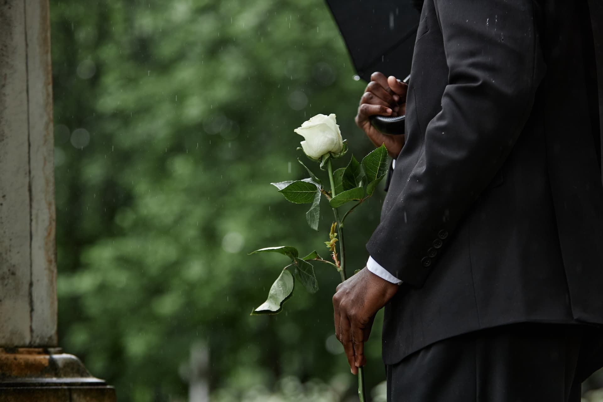 A man is holding a white rose in his hand at a funeral.