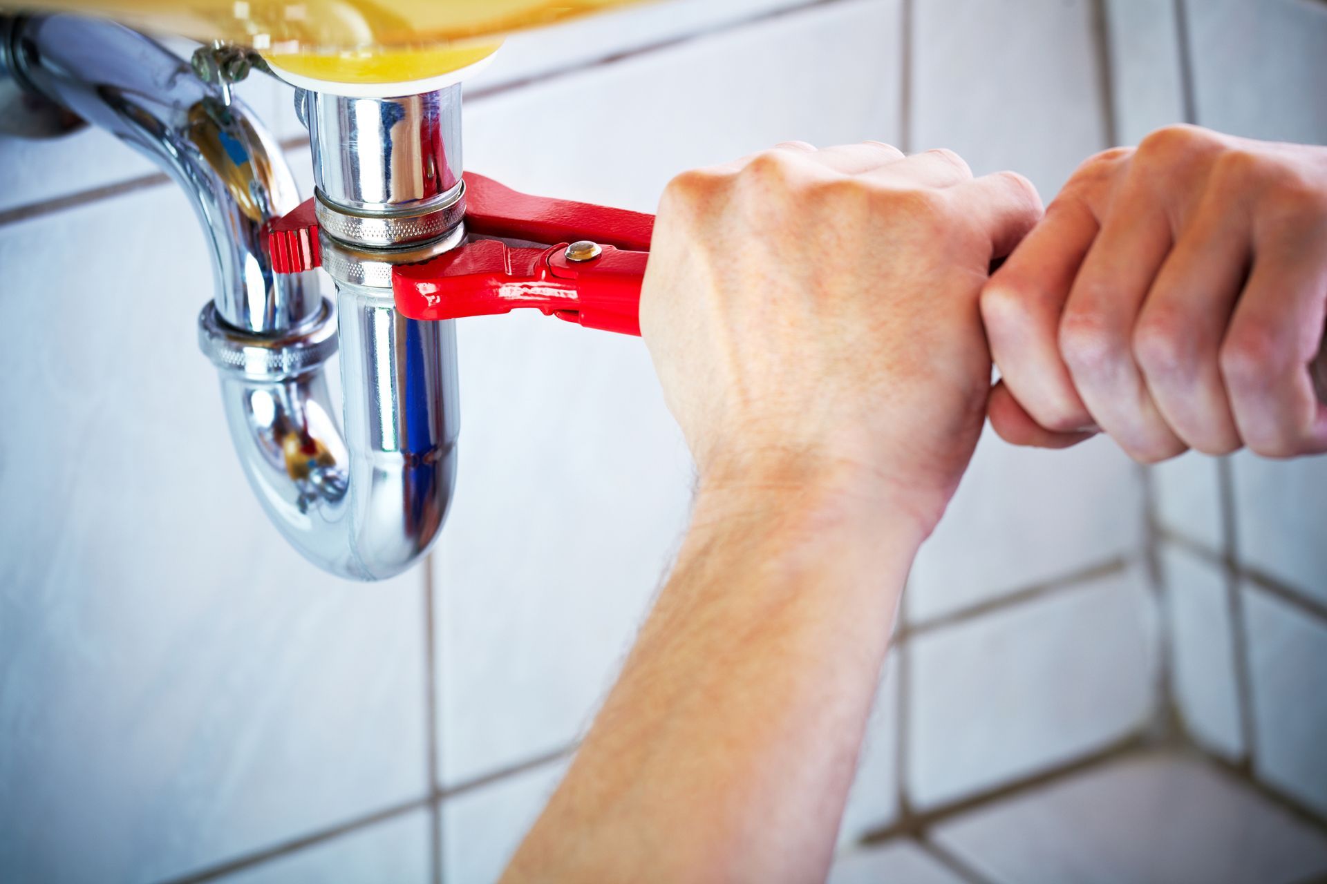 Plumber’s hands holding wrench fixing bathroom sink for clogged sink repair service efficiency.