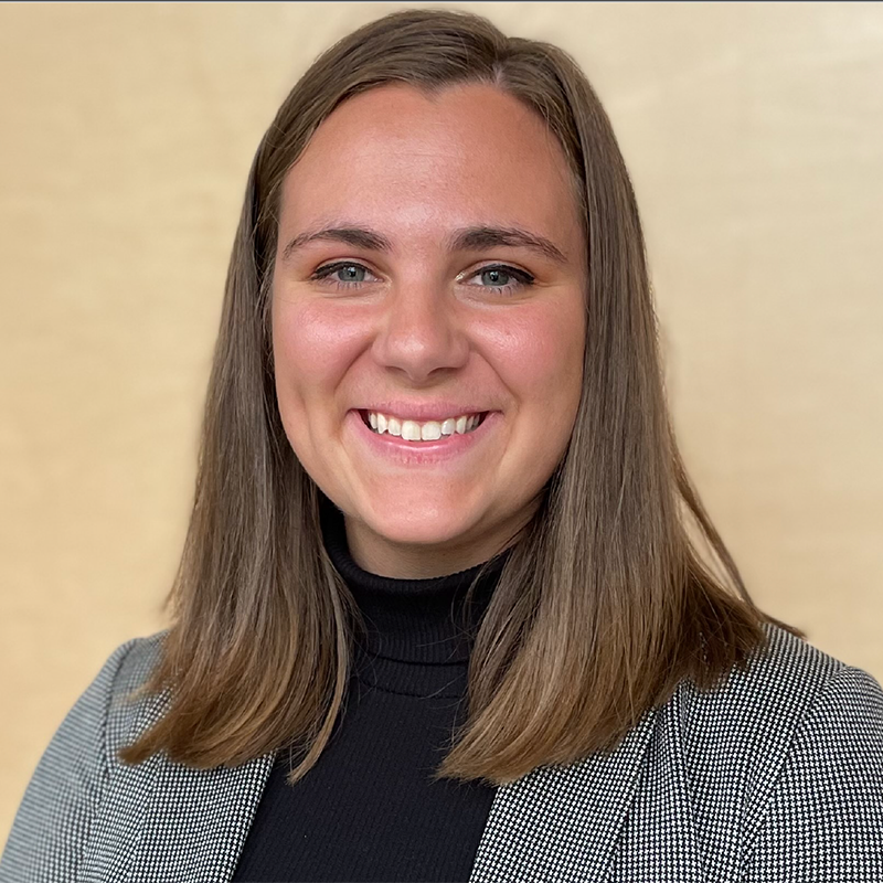 A woman wearing a black turtleneck and a plaid jacket is smiling for the camera.