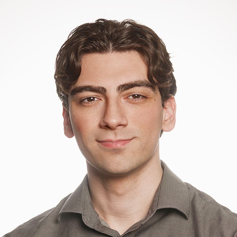 A young man wearing a black polo shirt is smiling for the camera