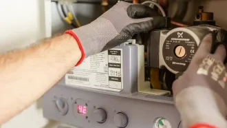 A man wearing gloves is working on a boiler.