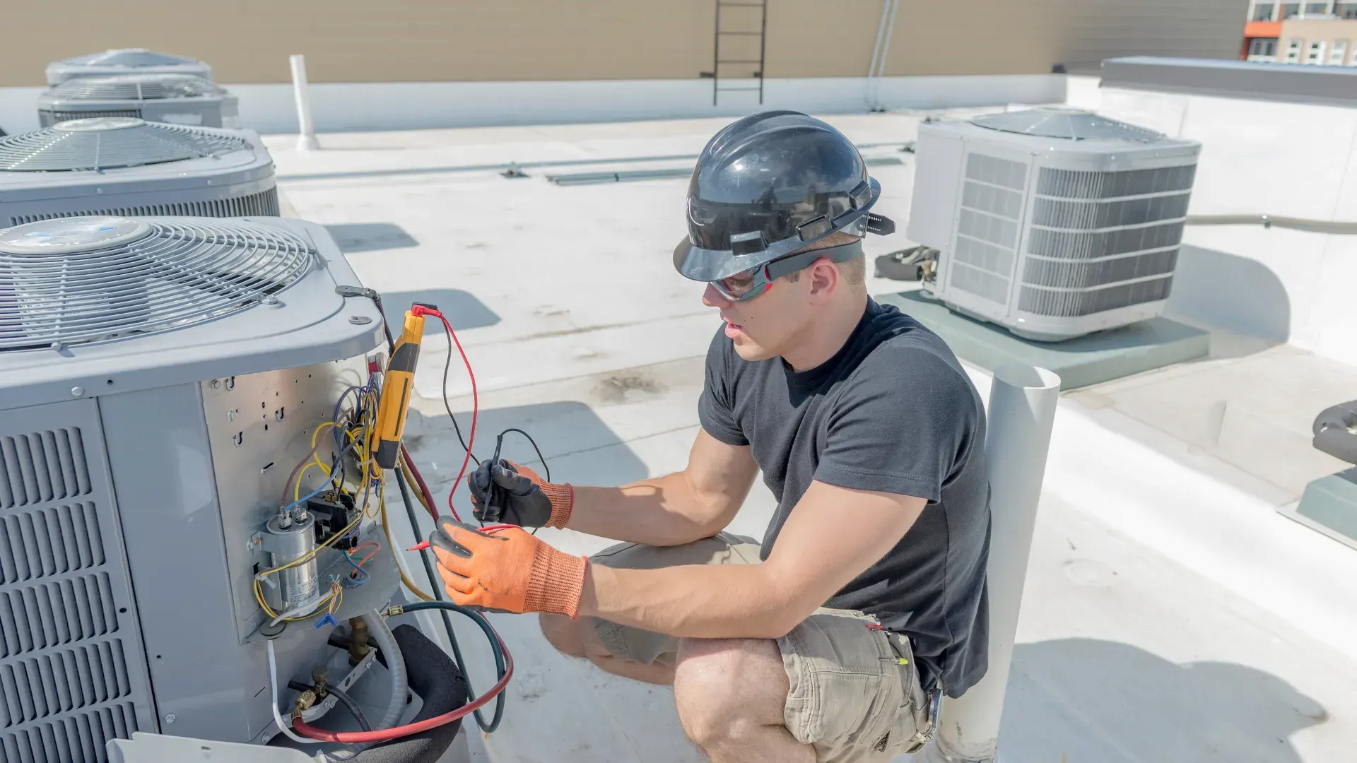 A man is working on an air conditioner on the roof of a building.